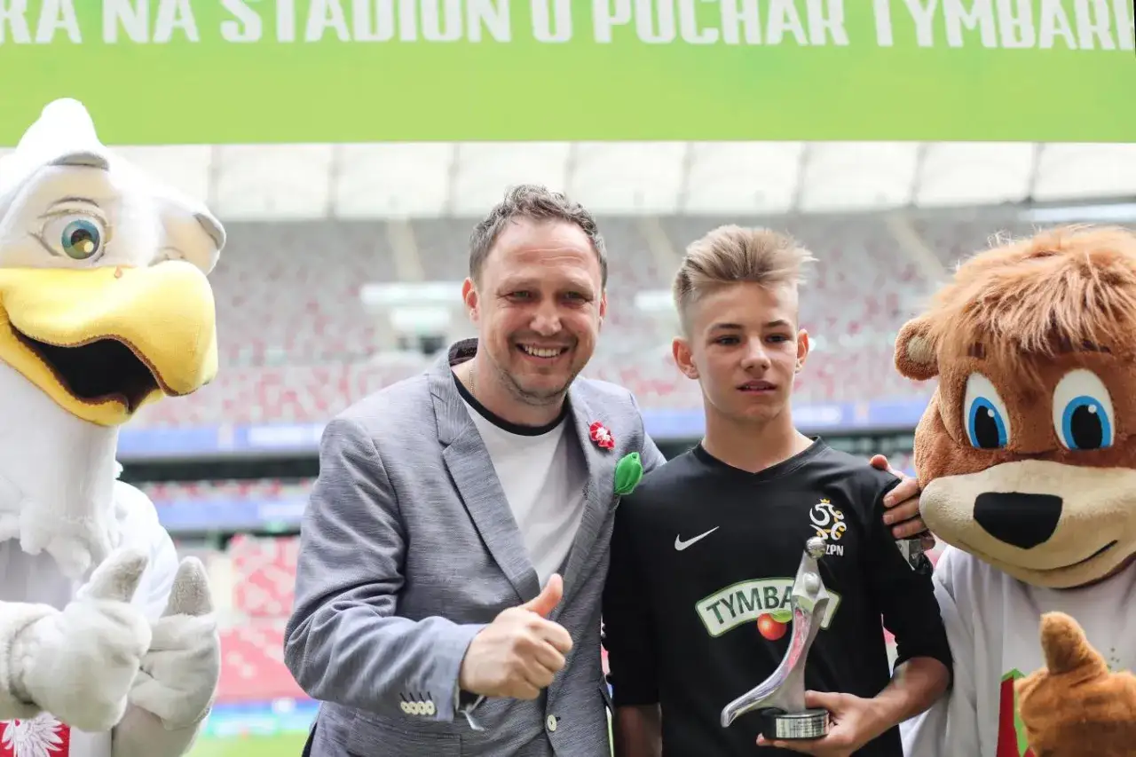Paweł Kryszałowicz z młodym piłkarzem i maskotkami na stadionie.