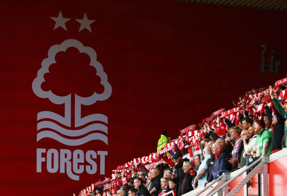 Trybuna kibiców Nottingham Forest podczas emocjonujących rozgrywek. W tle widnieje charakterystyczne logo klubu z drzewem i dwiema gwiazdami.