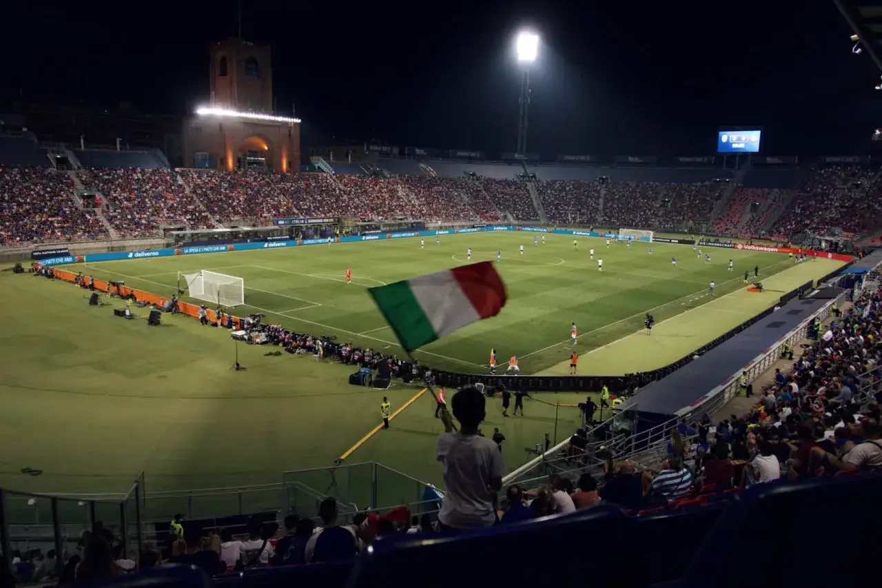 Nocny mecz na stadionie, kibic z flagą Włoch wspiera drużynę FC Bologna.