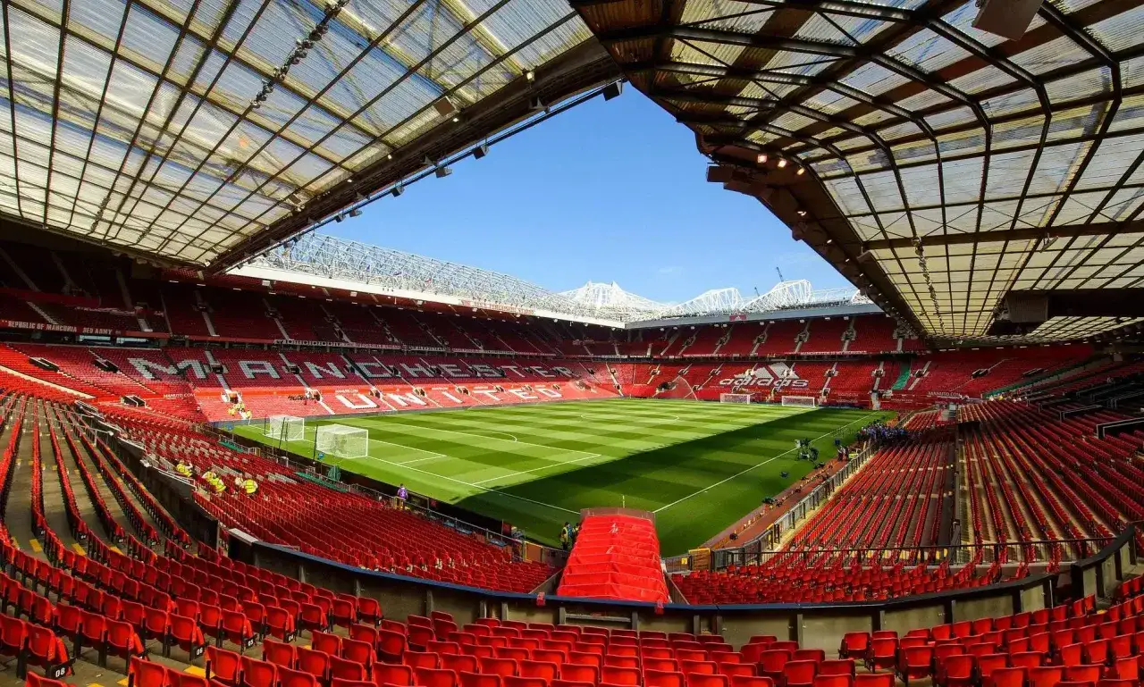 Pusta trybuna stadionu Old Trafford, gotowa na mecz Manchester United - Fulham. Czerwone krzesełka czekają na kibic&oacute;w.