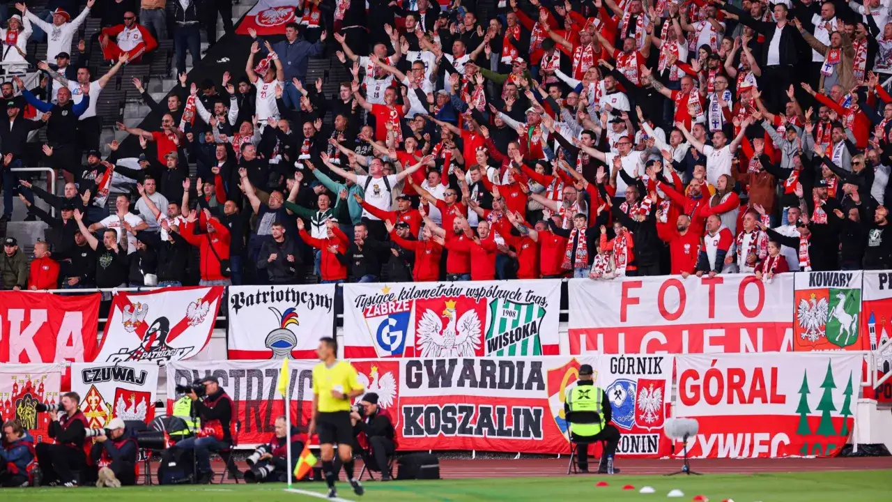 Tłum kibiców w biało-czerwonych barwach, z flagami i transparentami, wspiera polskich piłkarzy.