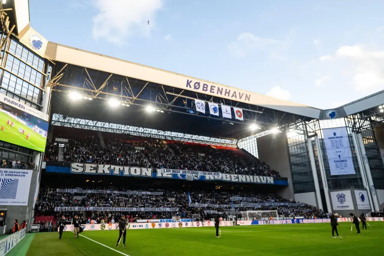 Stadion FC Kopenhaga podczas rozgrywek. Trybuny wypełnione kibicami, transparenty z napisami