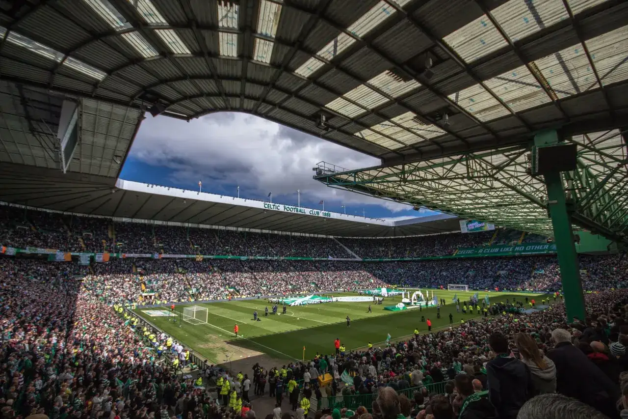 Trybuny stadionu Celtic Park wypełnione kibicami, gotowymi na emocjonujące rozgrywki. Zielono-białe barwy dominują, tworząc atmosferę święta futbolu.