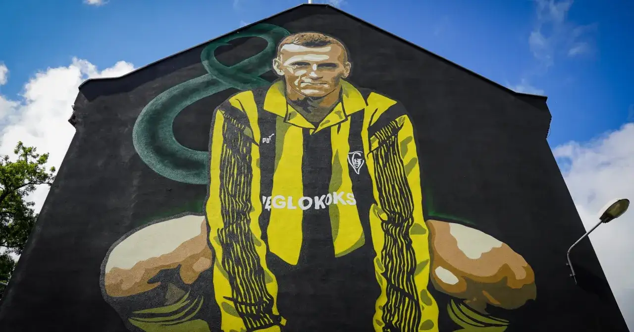 Mural z wizerunkiem Adama Ledwonia w żółto-czarnej koszulce piłkarskiej, z zielonym elementem w tle.