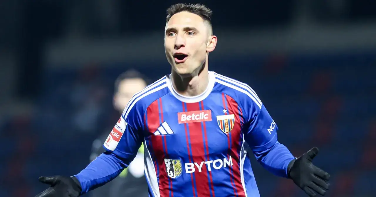 Piłkarz Jakub Arak w niebiesko-czerwonej koszulce z logo Betclic i Adidas, z otwartymi ramionami, świętuje bramkę.