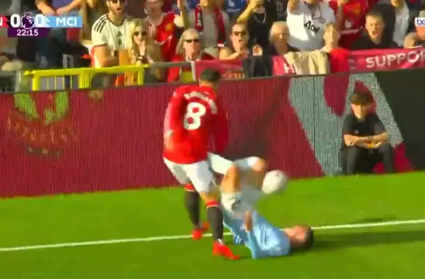 Piłkarz Manchesteru United w czerwonej koszulce z numerem 8 przewraca zawodnika Manchesteru City na murawę.