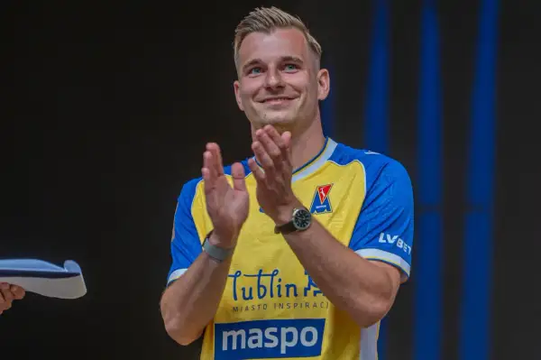 Uśmiechnięty Mateusz Legowski w żółto-niebieskiej koszulce z logo Motor Lublin klaszcze, świętując sukces.