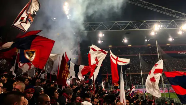 Tłum kibiców Genoa CFC z flagami na stadionie. Dym i światła tworzą atmosferę meczu.