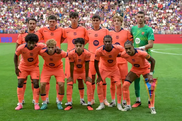 FC Barcelona - skład. Drużyna w pomarańczowych strojach pozuje do zdjęcia na boisku. W tle trybuny pełne kibiców.