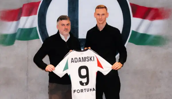 Rafał Adamski z numerem 9 na koszulce, obok niego mężczyzna, na tle flagi i logo klubu.
