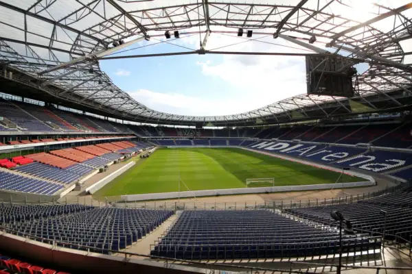 Pusta HDI Arena, stadion klubu Hannover 96, z zieloną murawą i rzędami niebieskich i czerwonych siedzeń pod przeszklonym dachem.