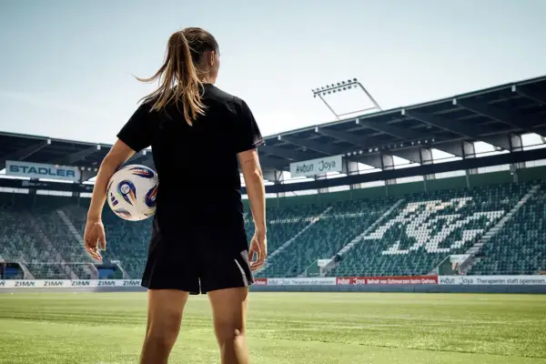 Dziewczyna z piłką nożną na tle stadionu, gotowa do gry.