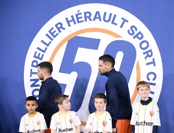 Piłkarze Montpellier HSC, klubu z ligi francuskiej, pozują z młodymi kibicami przed banerem z okazji 50-lecia klubu.
