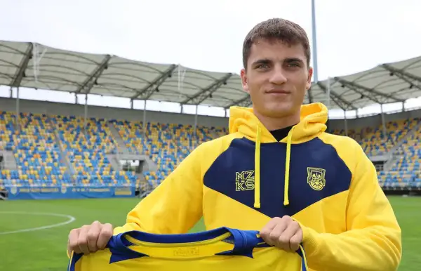 Filip Kocaba, młody piłkarz, prezentuje nowy strój na tle stadionu.